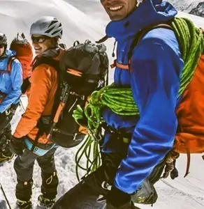 Team of mountaineers smiling and ready to climb in high-altitude snow environment, wearing bright technical gear and carrying neon green climbing ropes. Alpine trekking, winter adventure, and outdoor sports.