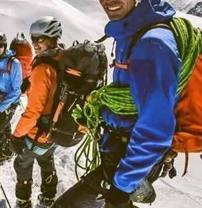 Team of mountaineers smiling and ready to climb in high-altitude snow environment, wearing bright technical gear and carrying neon green climbing ropes. Alpine trekking, winter adventure, and outdoor sports.