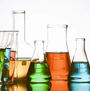 An assortment of laboratory glassware, including beakers, Erlenmeyer flasks, and test tubes, containing brightly colored chemical liquids. Science, research and development (R&D), and chemistry visual.